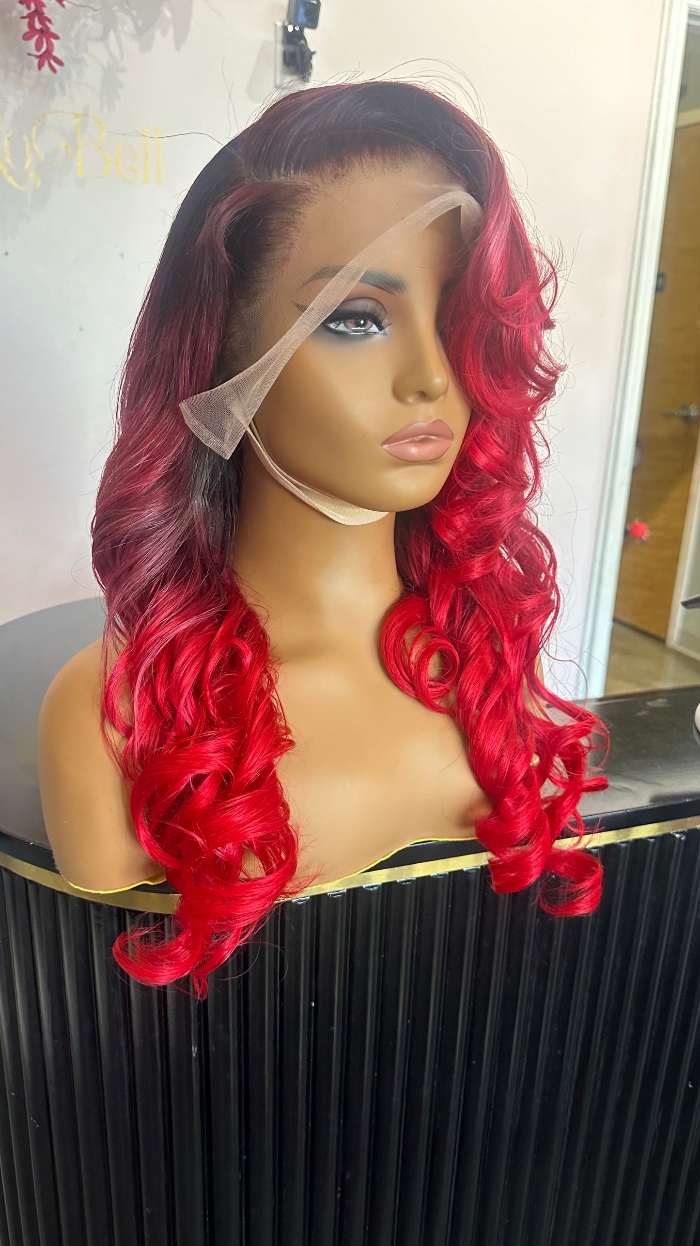 Human hair wig that is primarily a ruby red color with darker roots; front left quarter view.