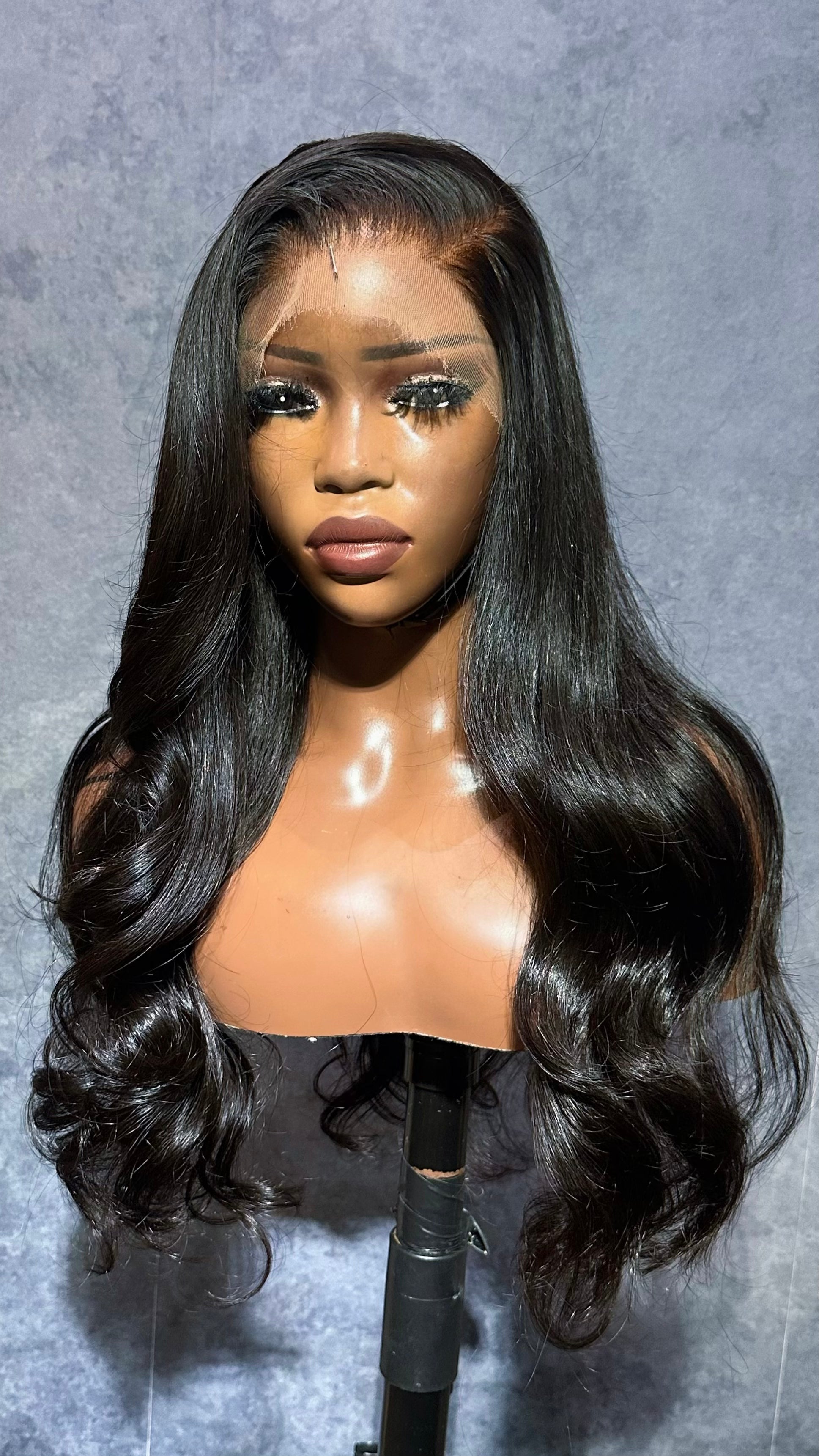 Black wig on a mannequin head against a gray background